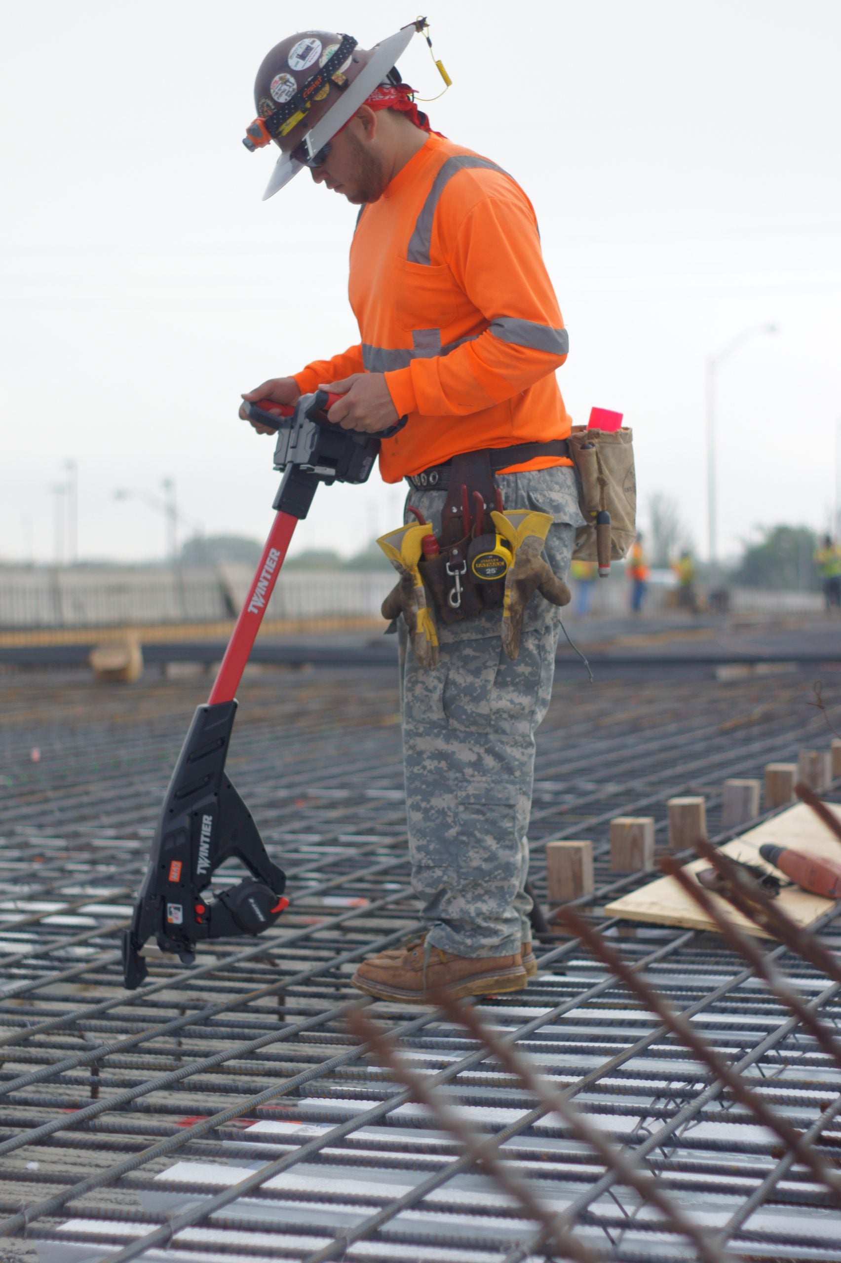 Cordless rebar tying tool held by worker; red handle and black head